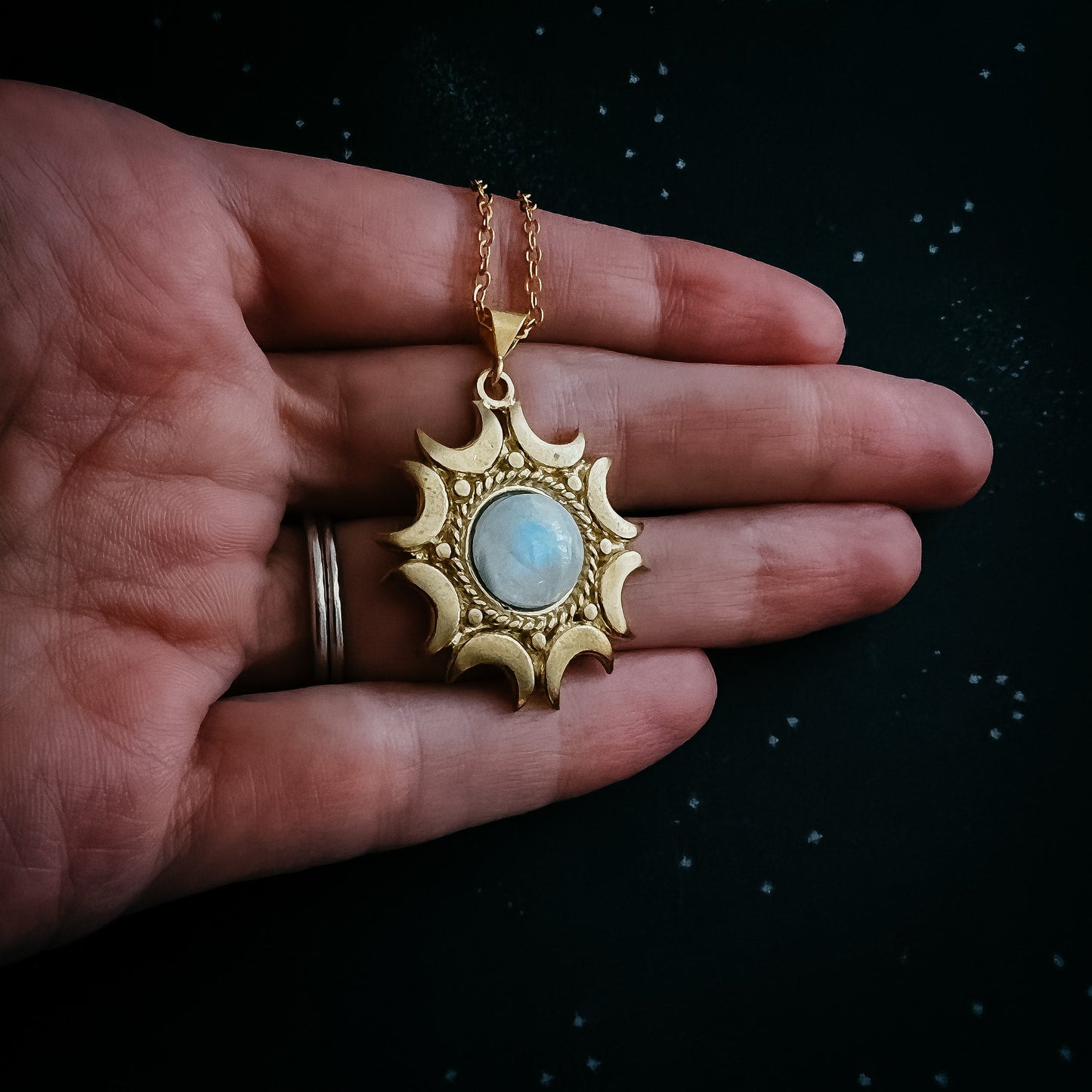 Gold pendant with a moonstone held in a hand against a dark background