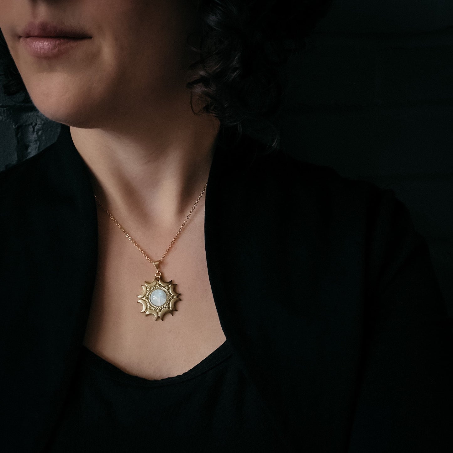 Woman wearing a gold necklace with a pendant against a dark background