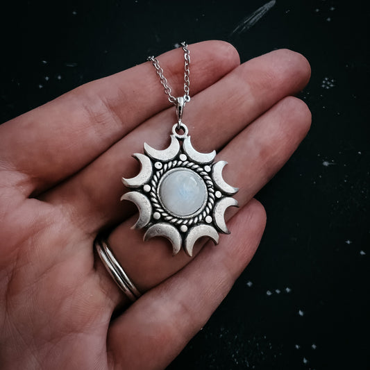 Silver Moonstone pendant necklace held in a hand against a dark background