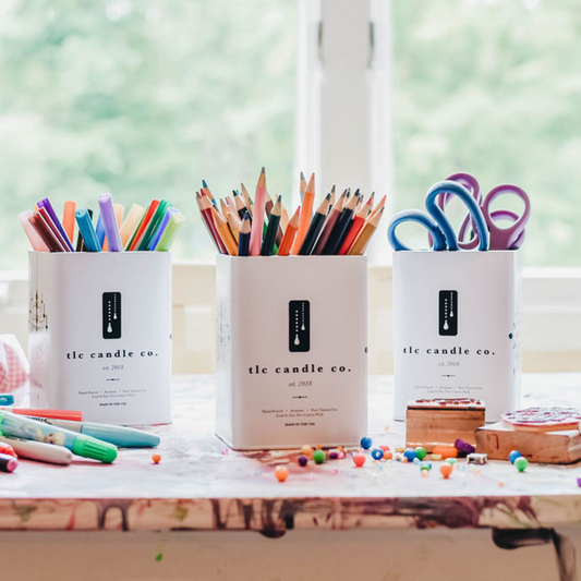 Three candle containers from 'tle candle co.' filled with stationery items on a desk.