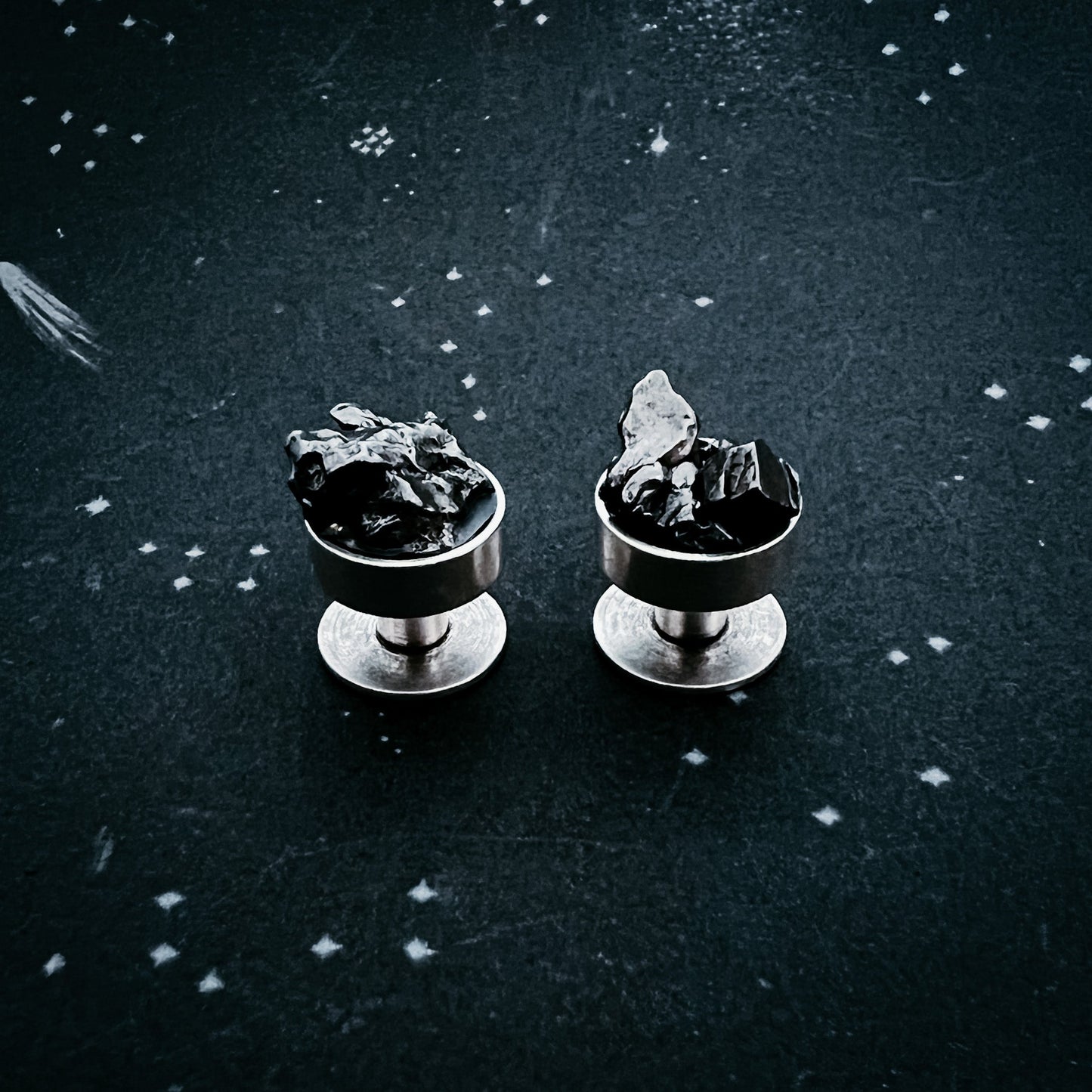 Two cufflinks with meteorites on a dark textured background