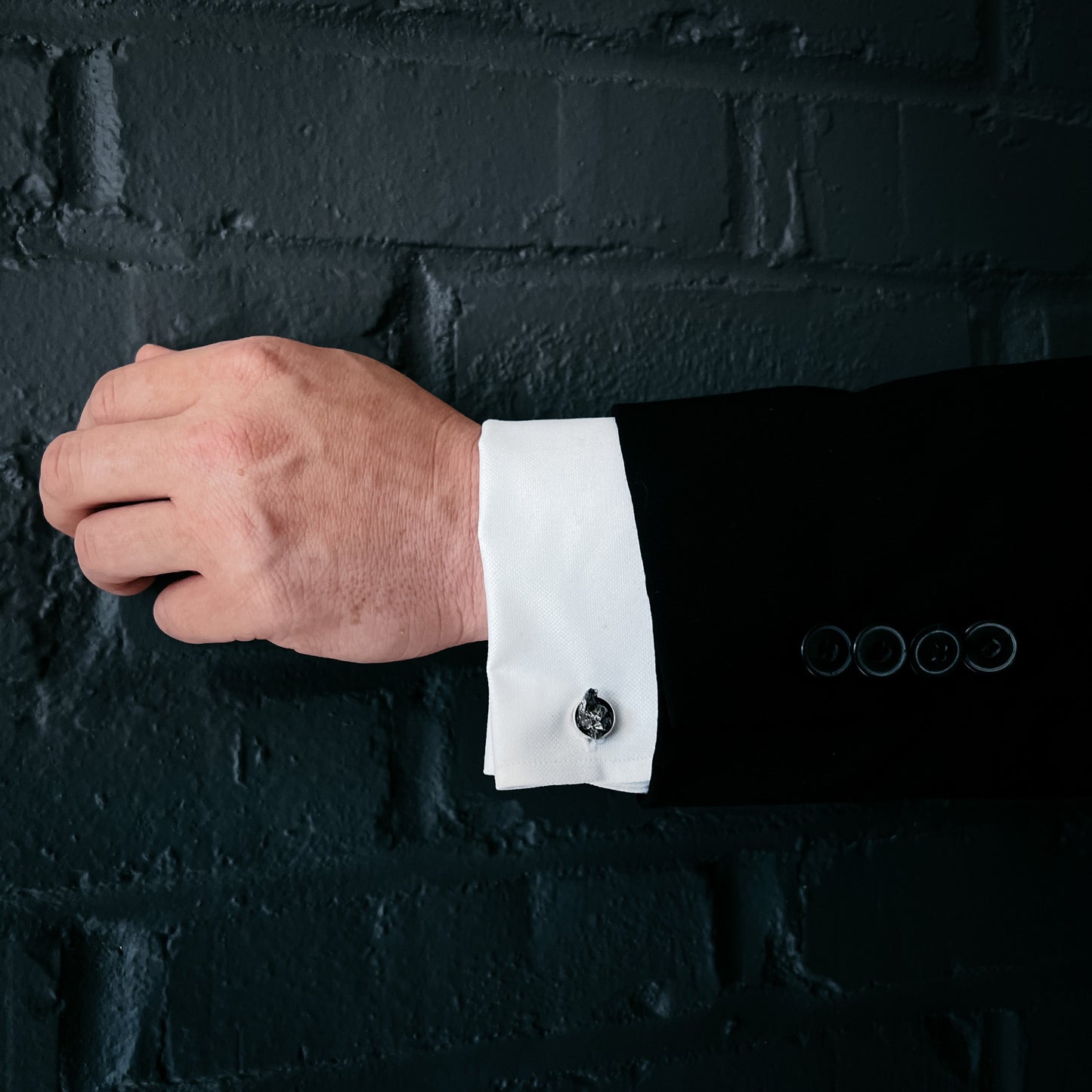 Cufflink on a white cuff against a dark brick wall