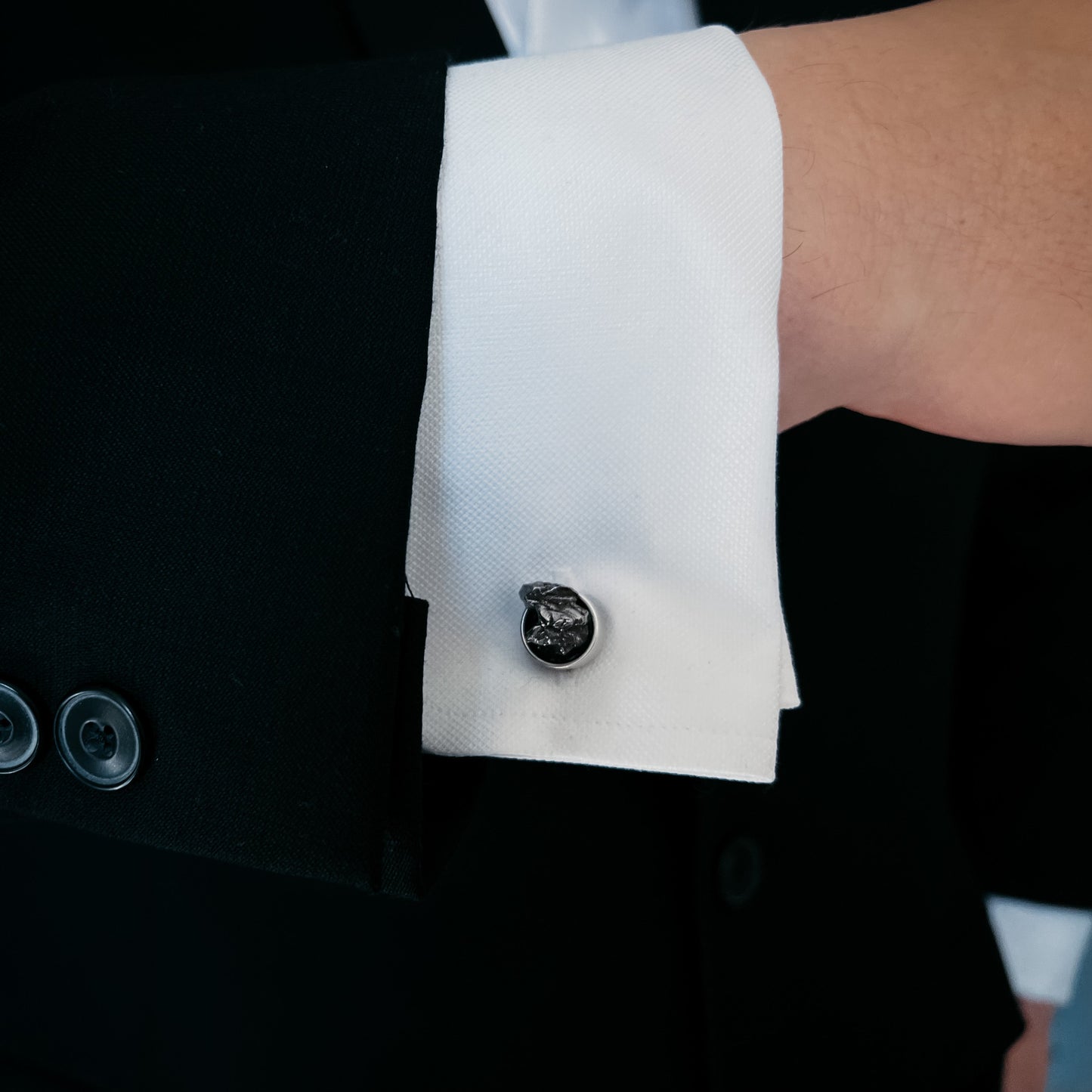 Close-up of a cufflink on a white cuff against a black suit background