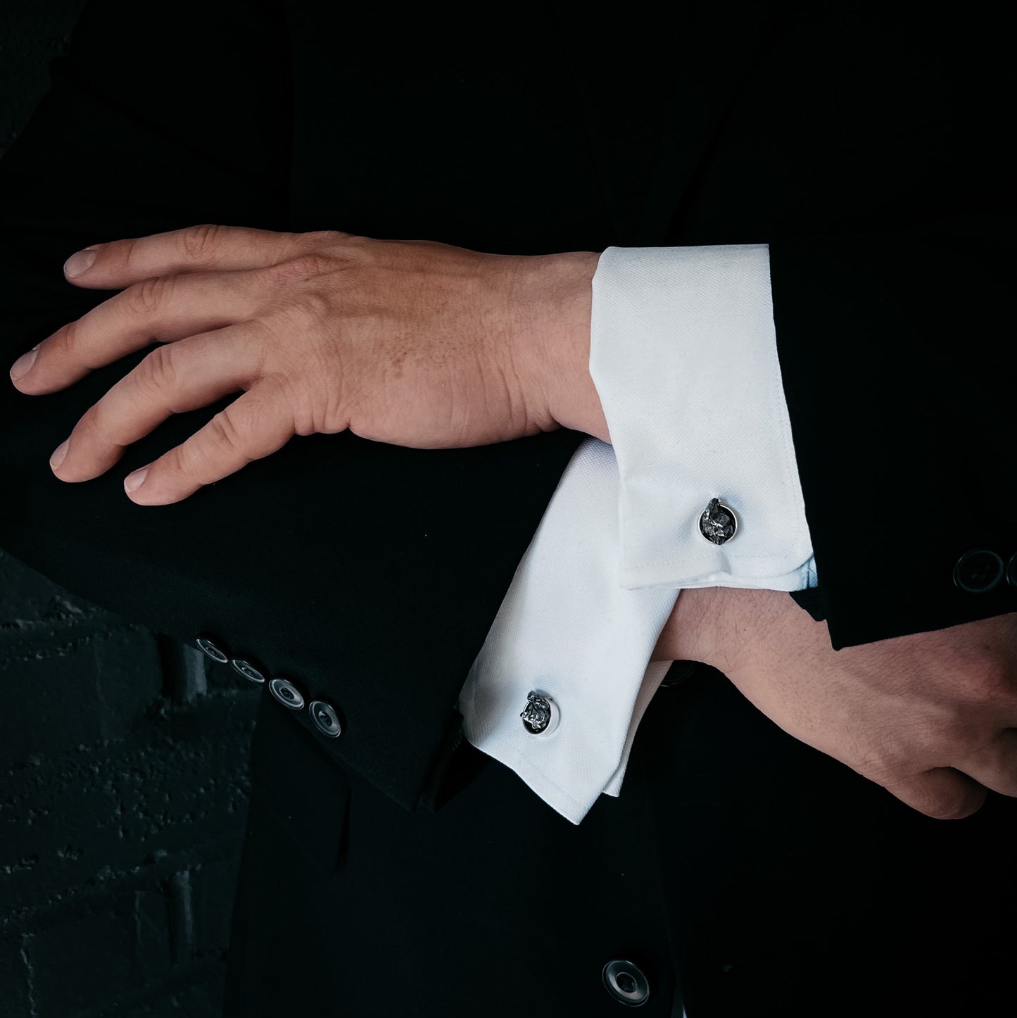 Close-up of a person adjusting a cuff on a black suit jacket.
