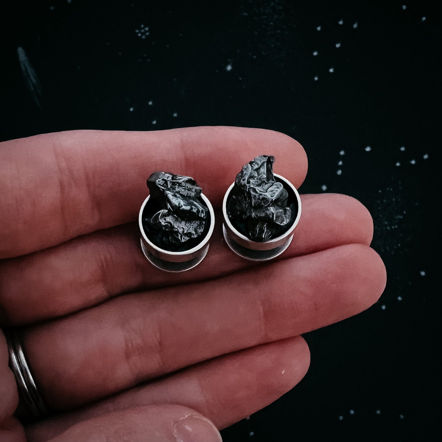 Pair of meteorite cufflinks held between fingers against a dark background