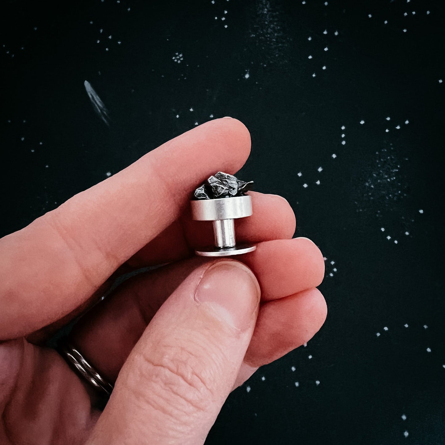 Hand holding a meteorite cufflink against a starry night sky background