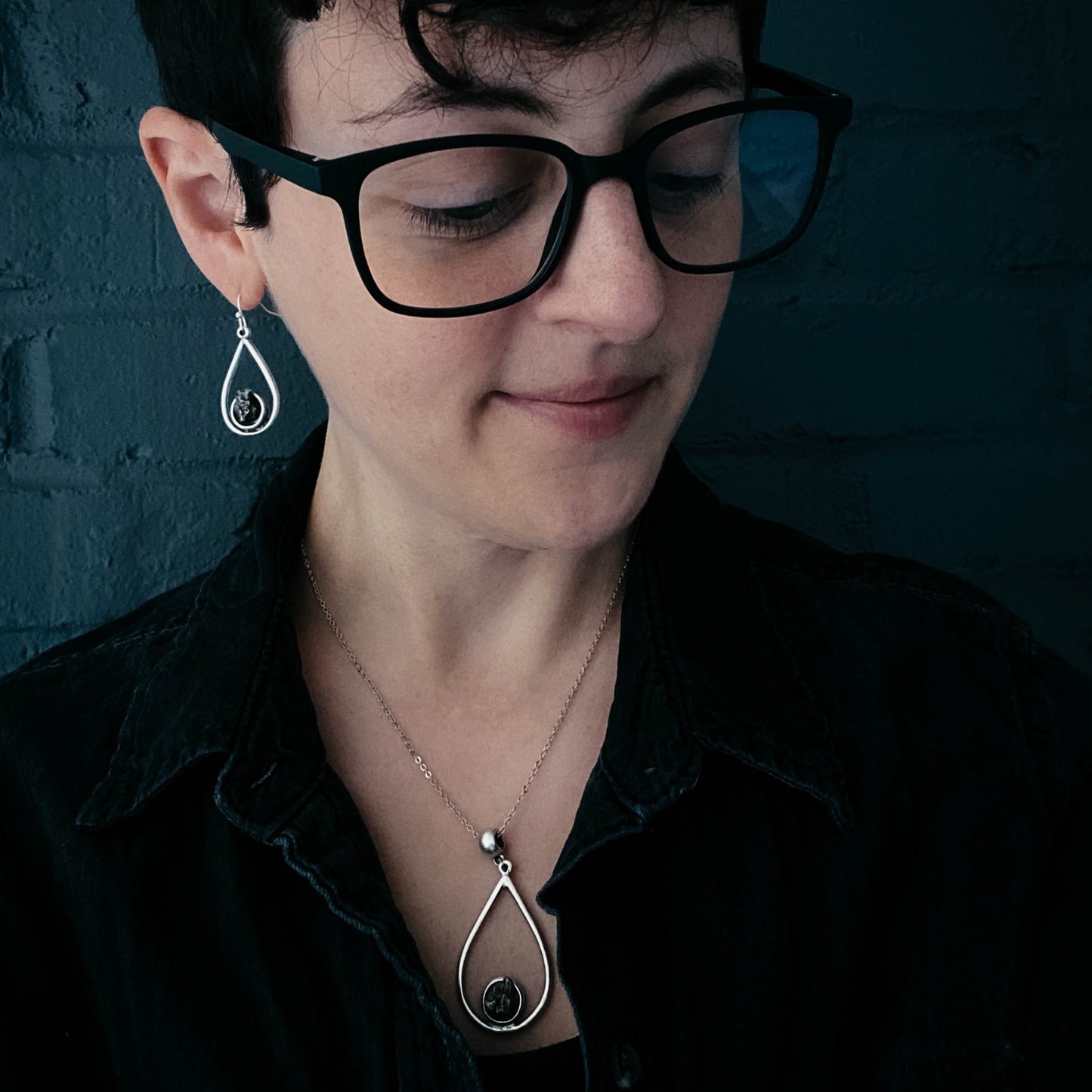Woman wearing black glasses and a black shirt with a dark background