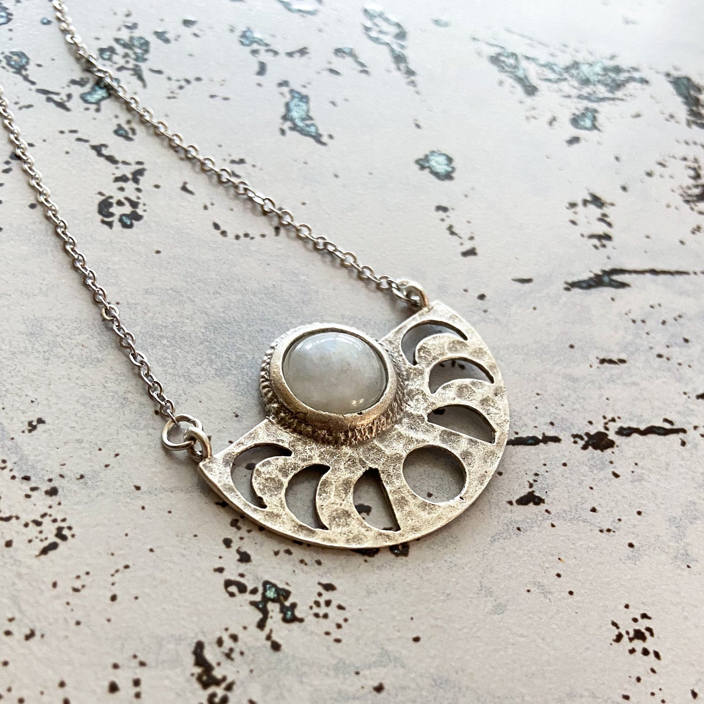 Silver tone necklace with a circular pendant on a textured surface