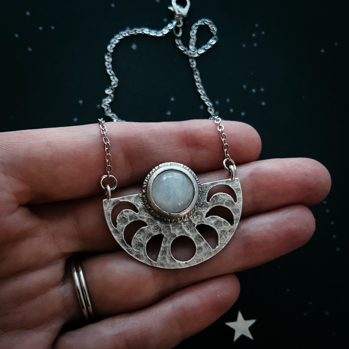 Silver necklace with a pendant held in a hand against a dark background