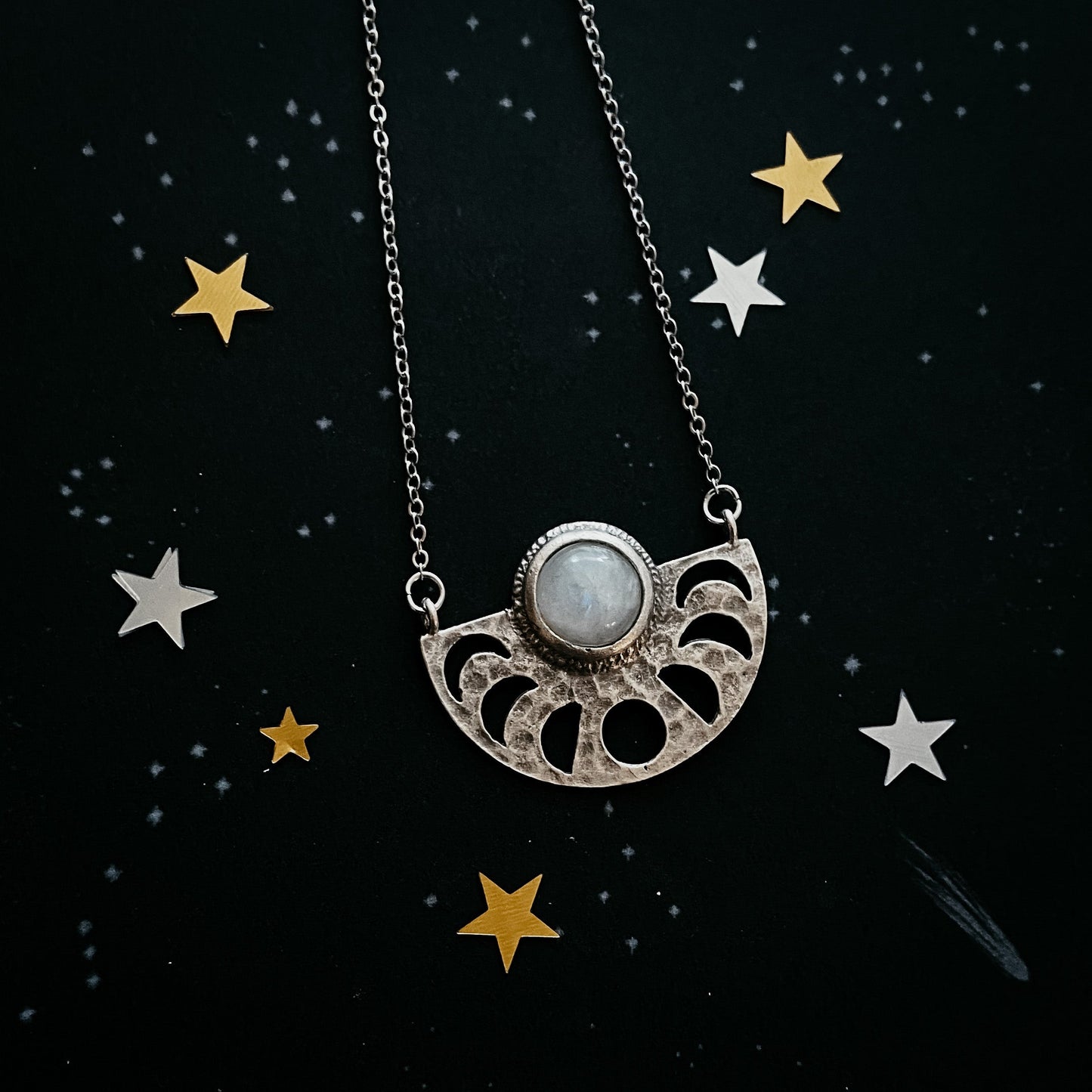Silver necklace with a moonstone pendant on a dark background with star decorations