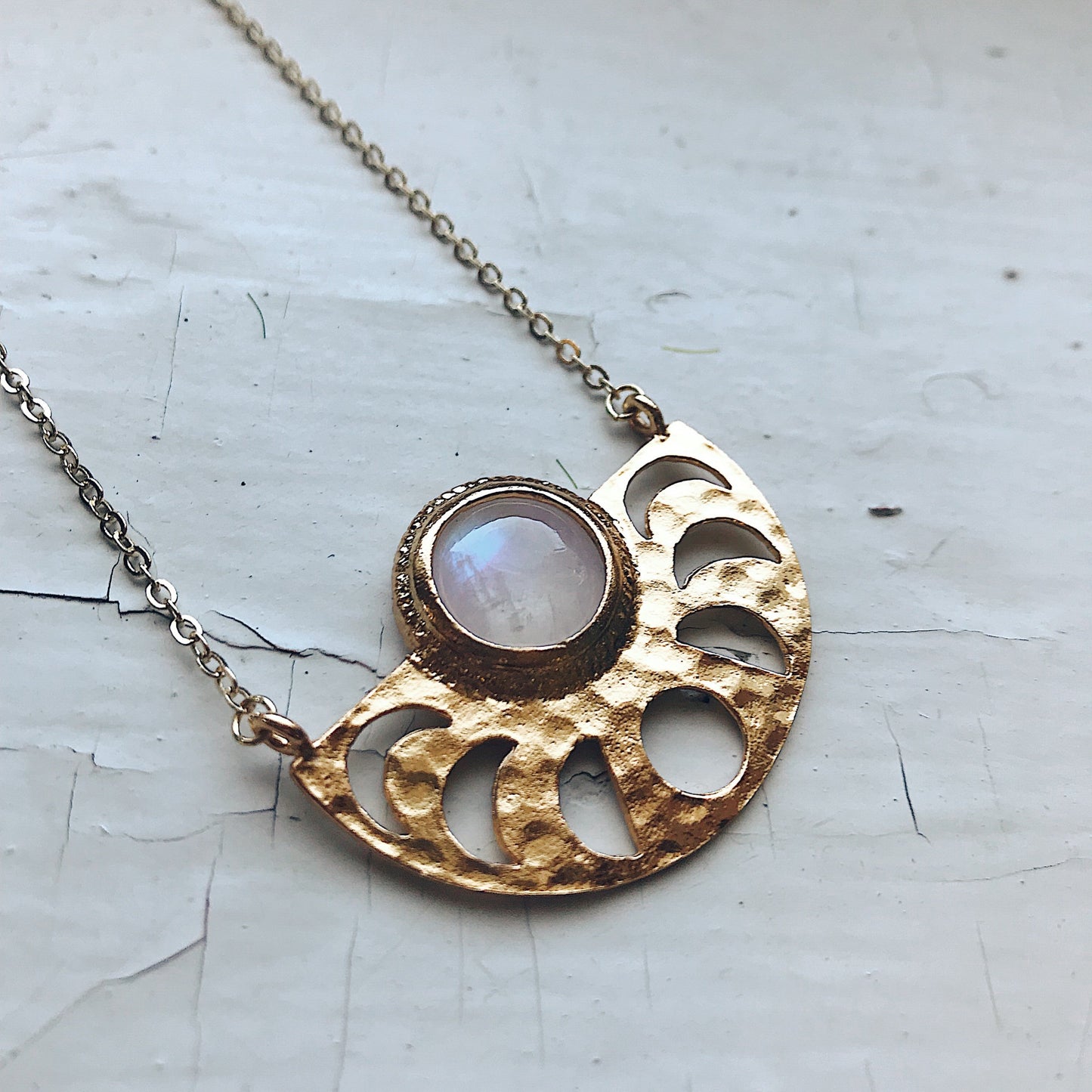 Gold tone necklace with a moonstone pendant on a textured white background