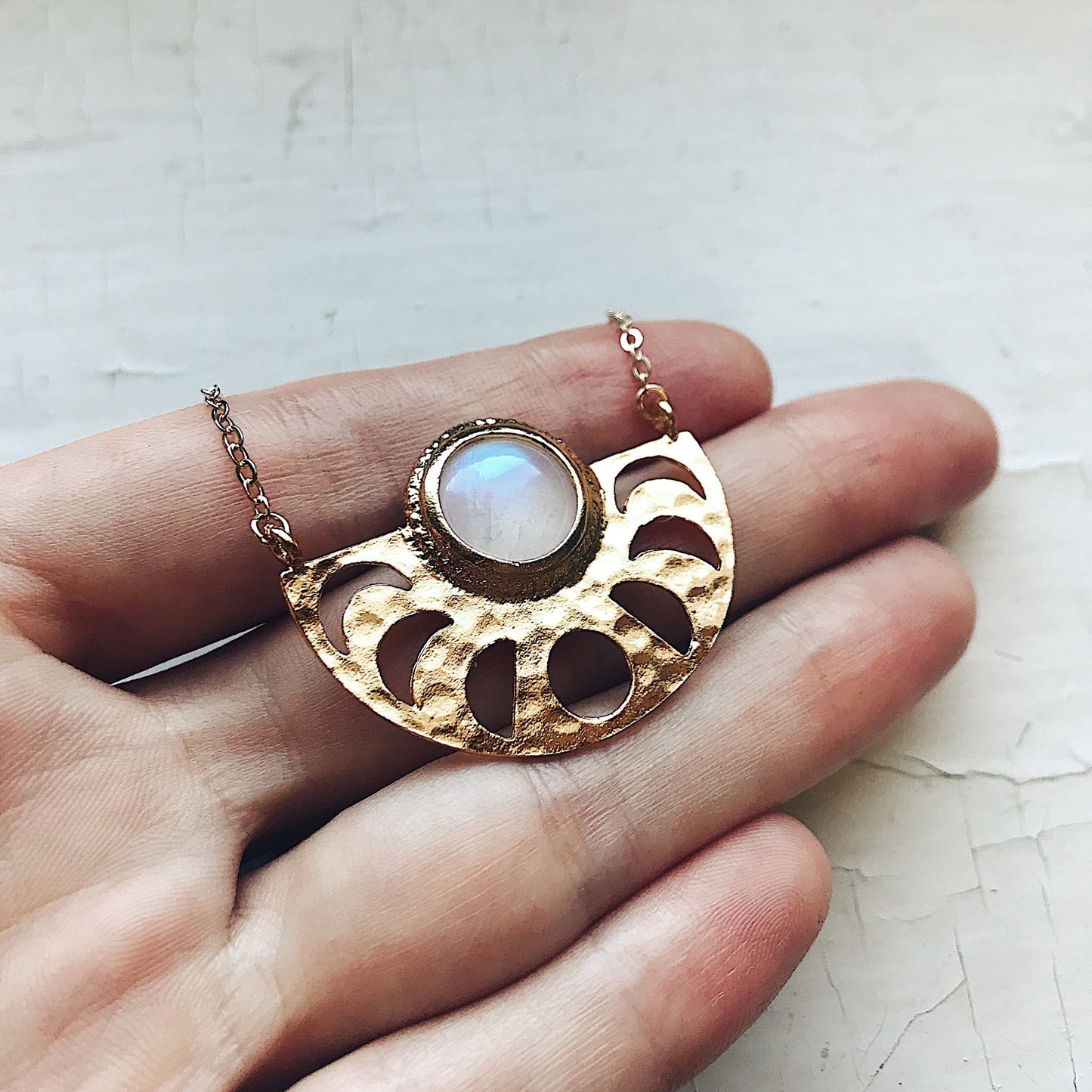 Gold necklace with a moonstone pendant held in a hand on a textured surface