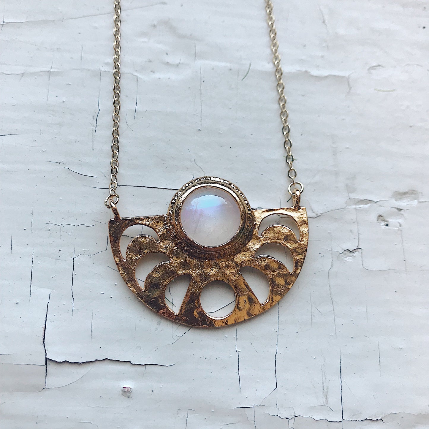 Gold necklace with a central gemstone on a textured white background