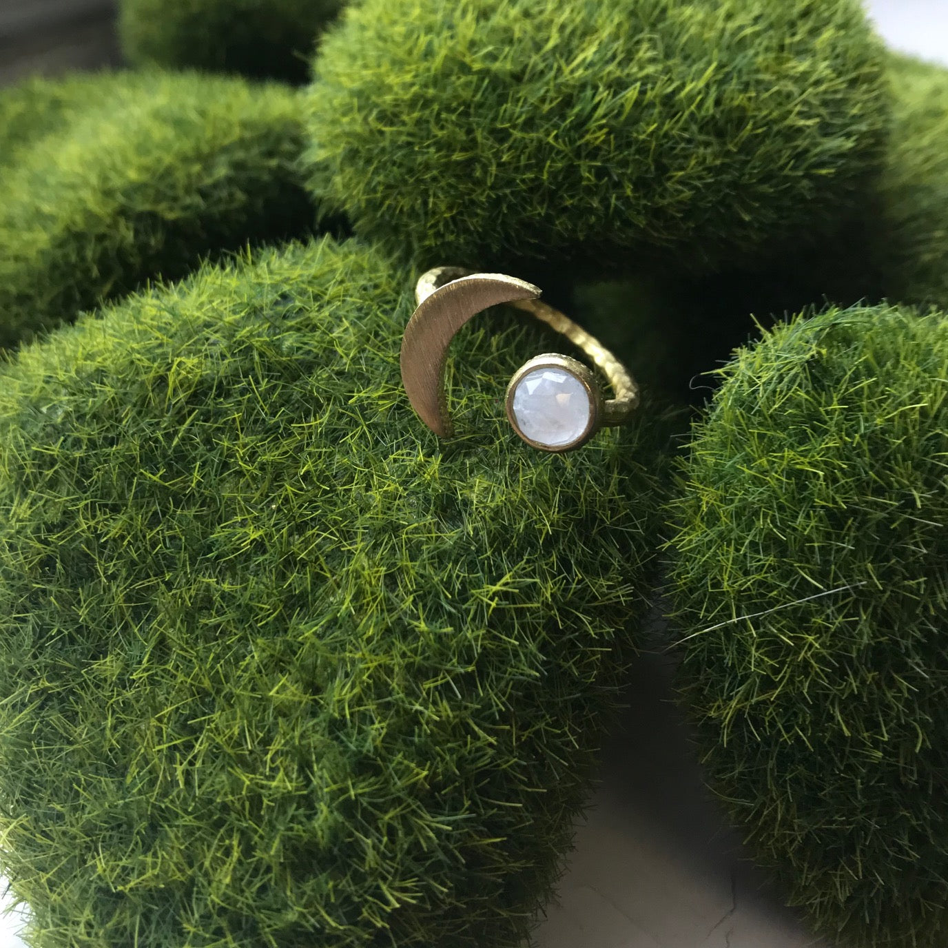 Gold ring with a white stone on a green textured surface