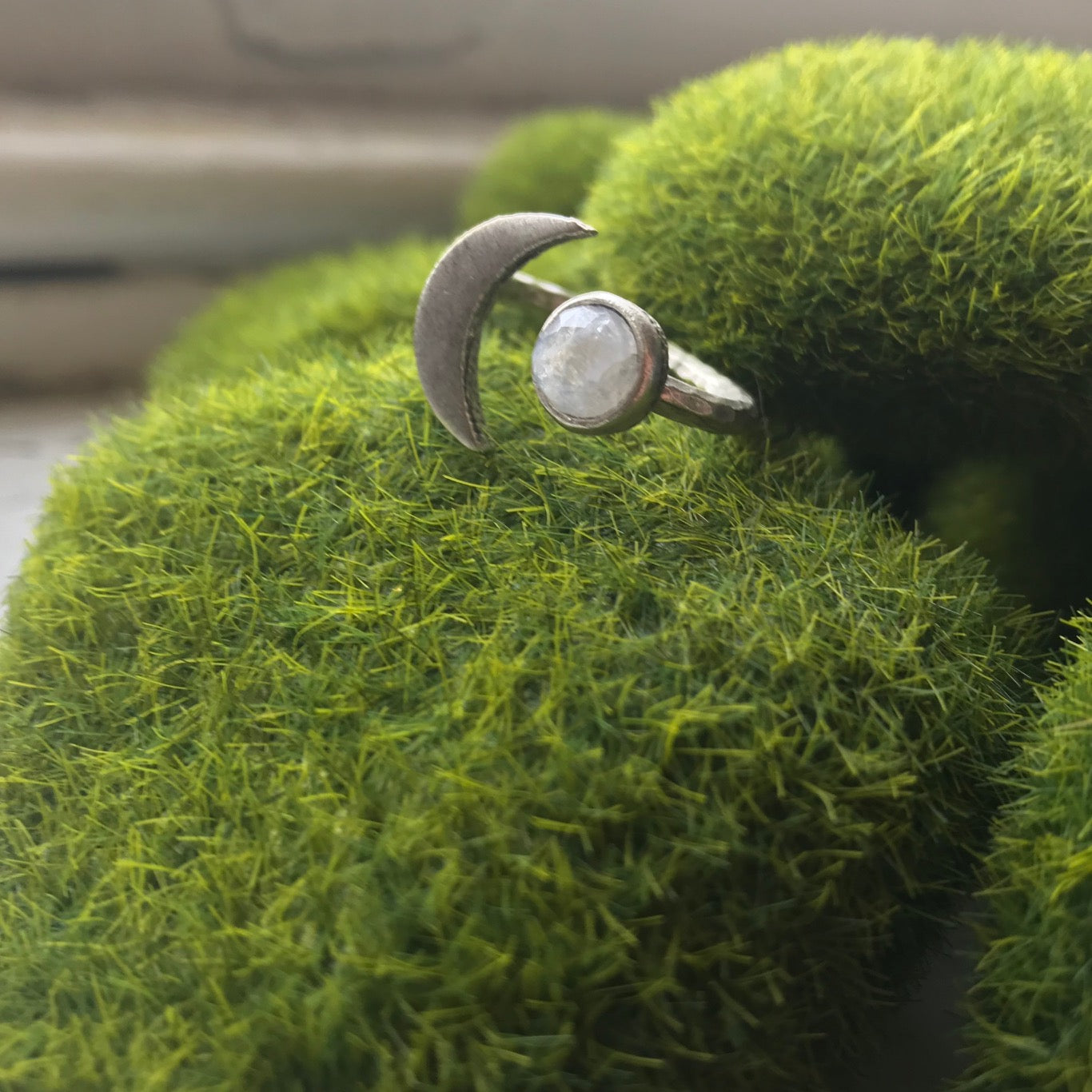 Silver ring with a moon design on a green textured surface