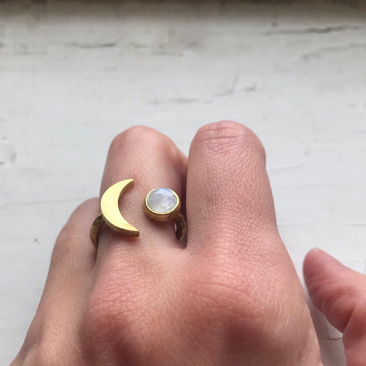 Gold ring with a moon design on a finger against a light background