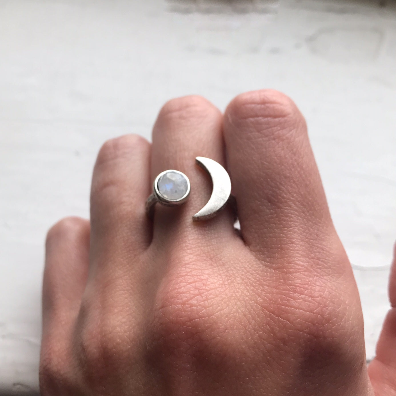 Hand wearing two rings with a moon design on a light background