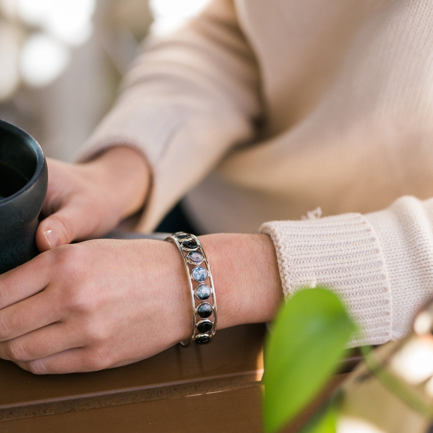 Person holding a black mug with a bracelet on a blurred background