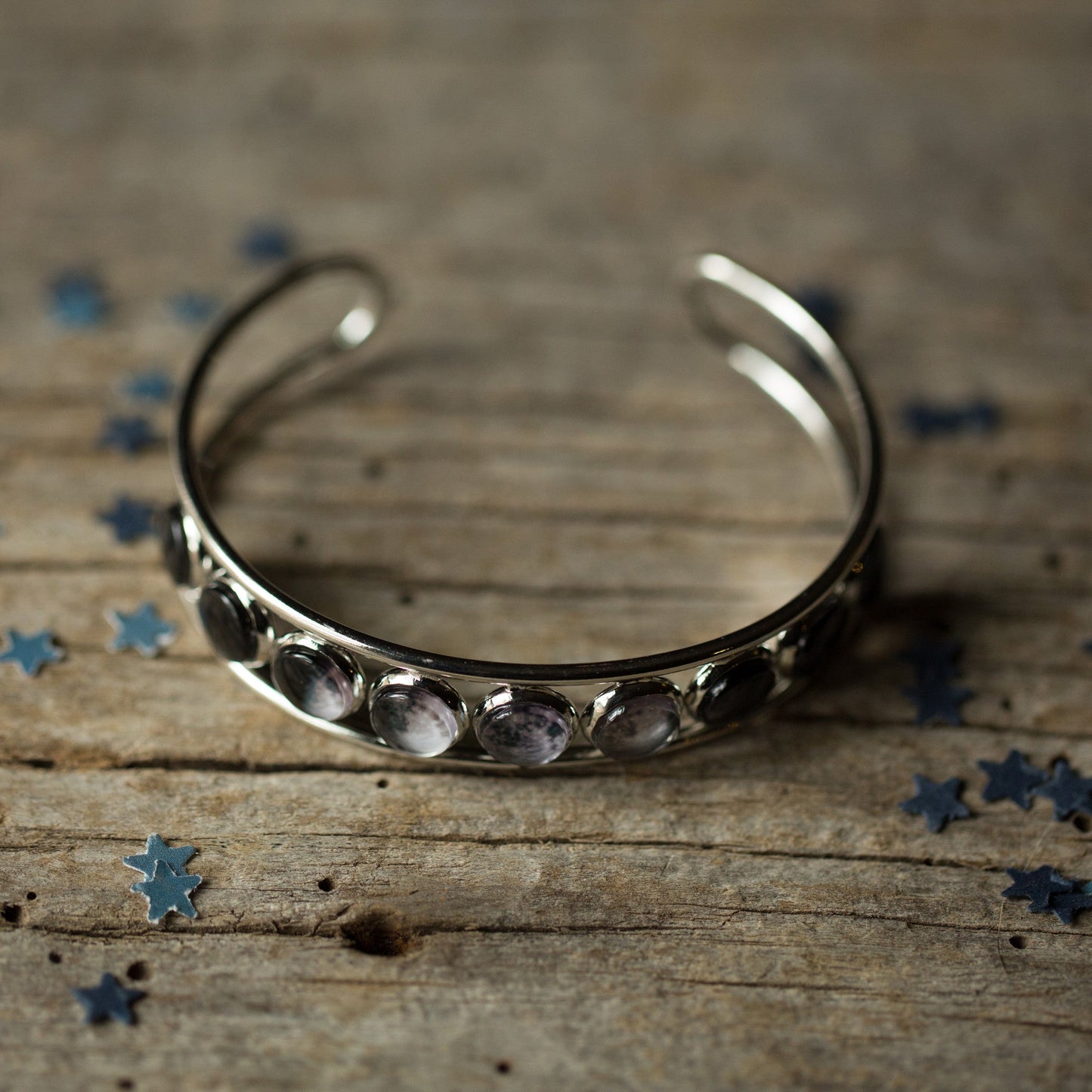 Silver bracelet with embedded stones on a wooden surface with scattered blue stars.