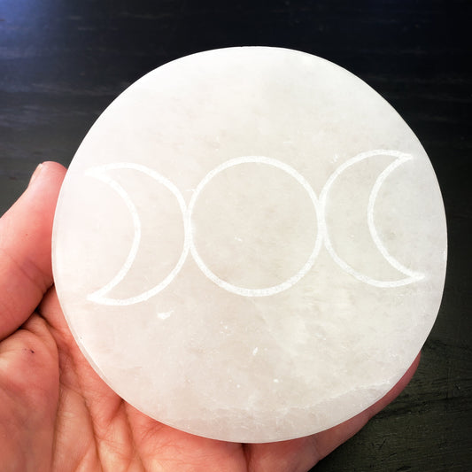 Selenite plate engraved with moon phase symbols held in a hand against a dark background