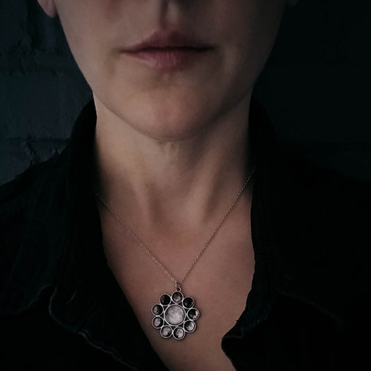 Close-up of a woman wearing a necklace with a detailed pendant against a dark background
