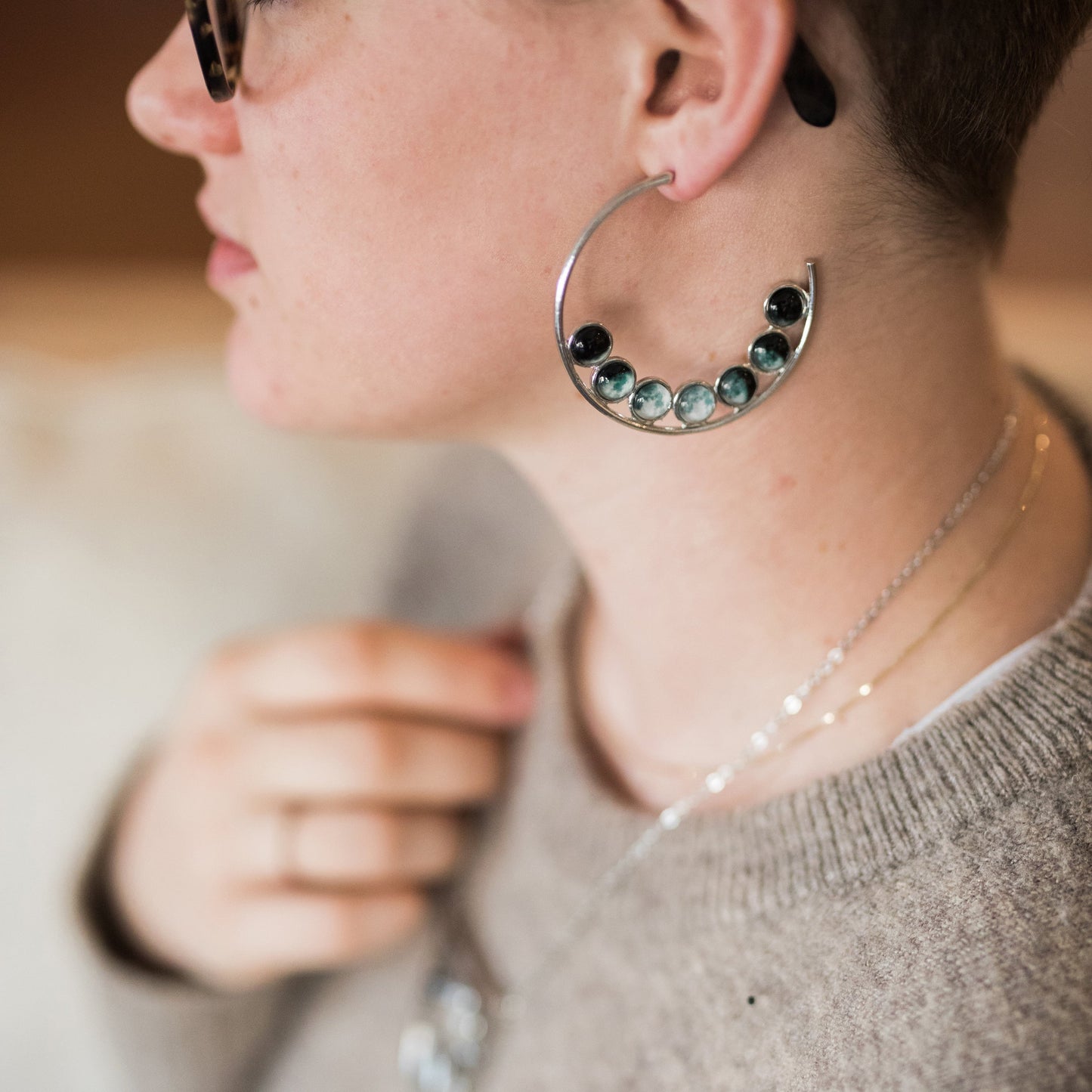 Close-up of a person wearing a silver hoop earring with green gemstones.