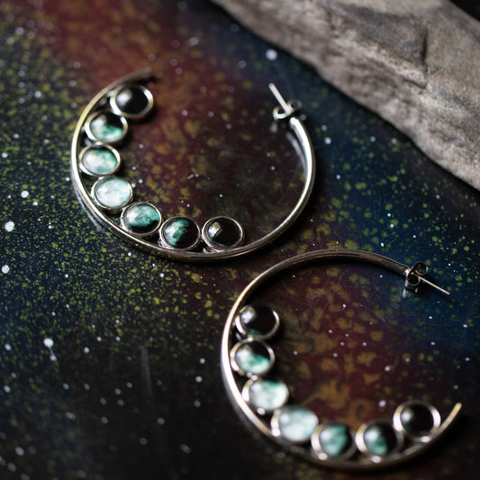 Pair of earrings with green gemstones on a dark, textured surface