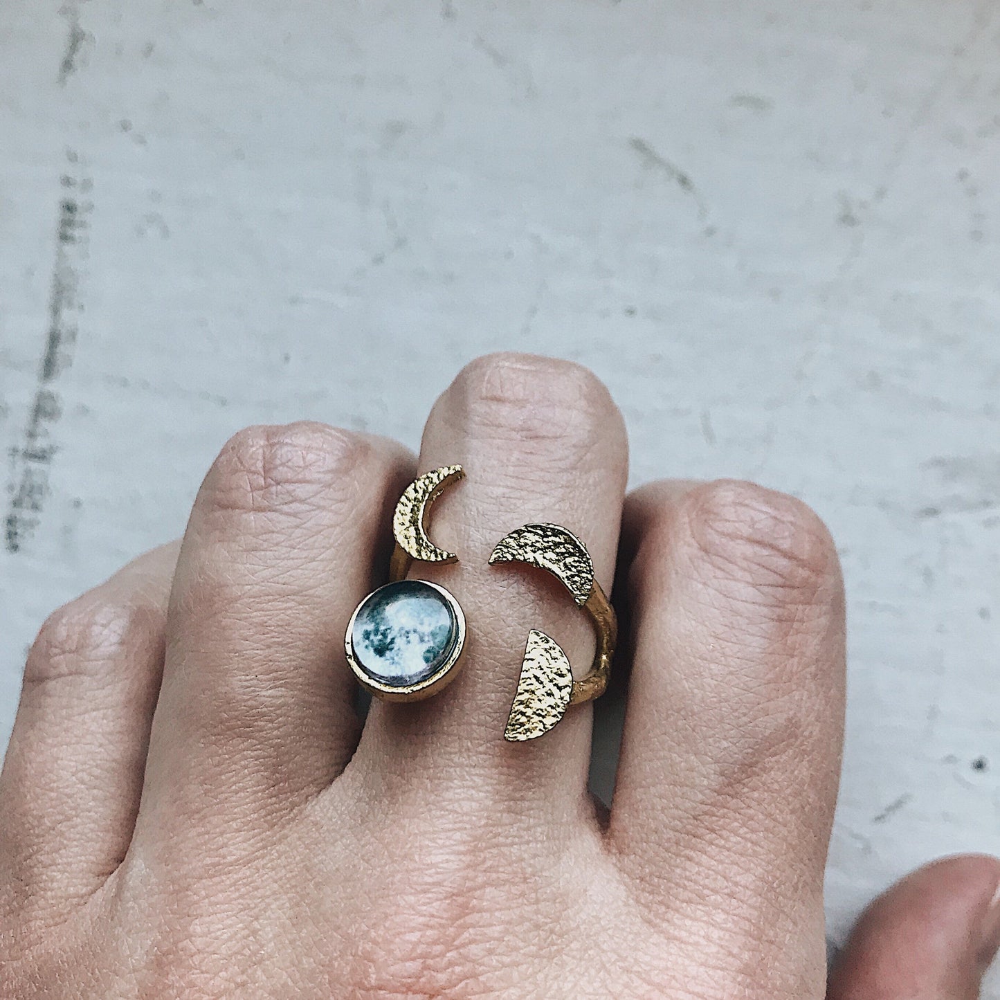Gold tone ring with moon design on a finger against a neutral background