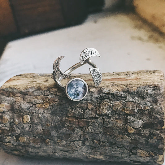 Silver tone ring with moon and star design on a wooden surface