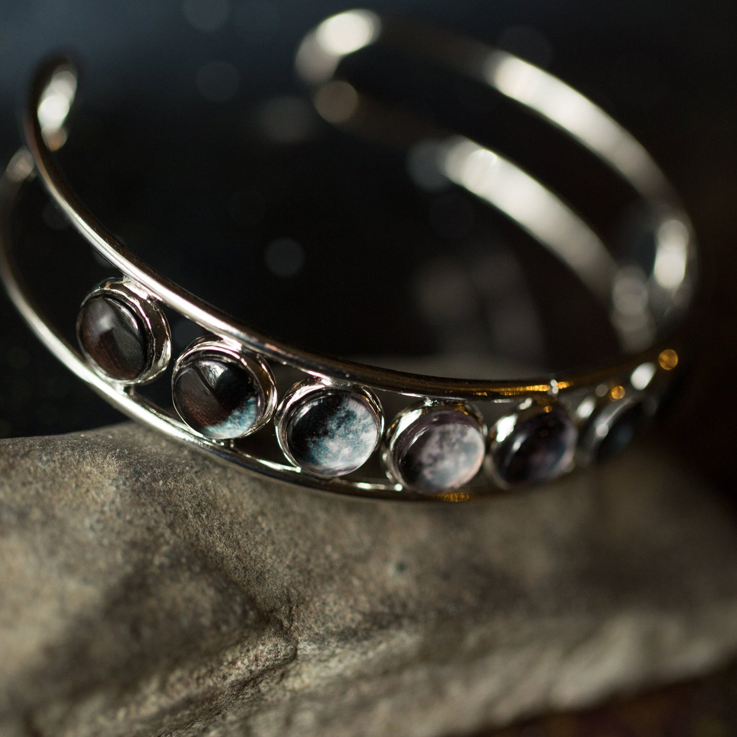Silver adjustable cuff bracelet with embedded stones on a dark background