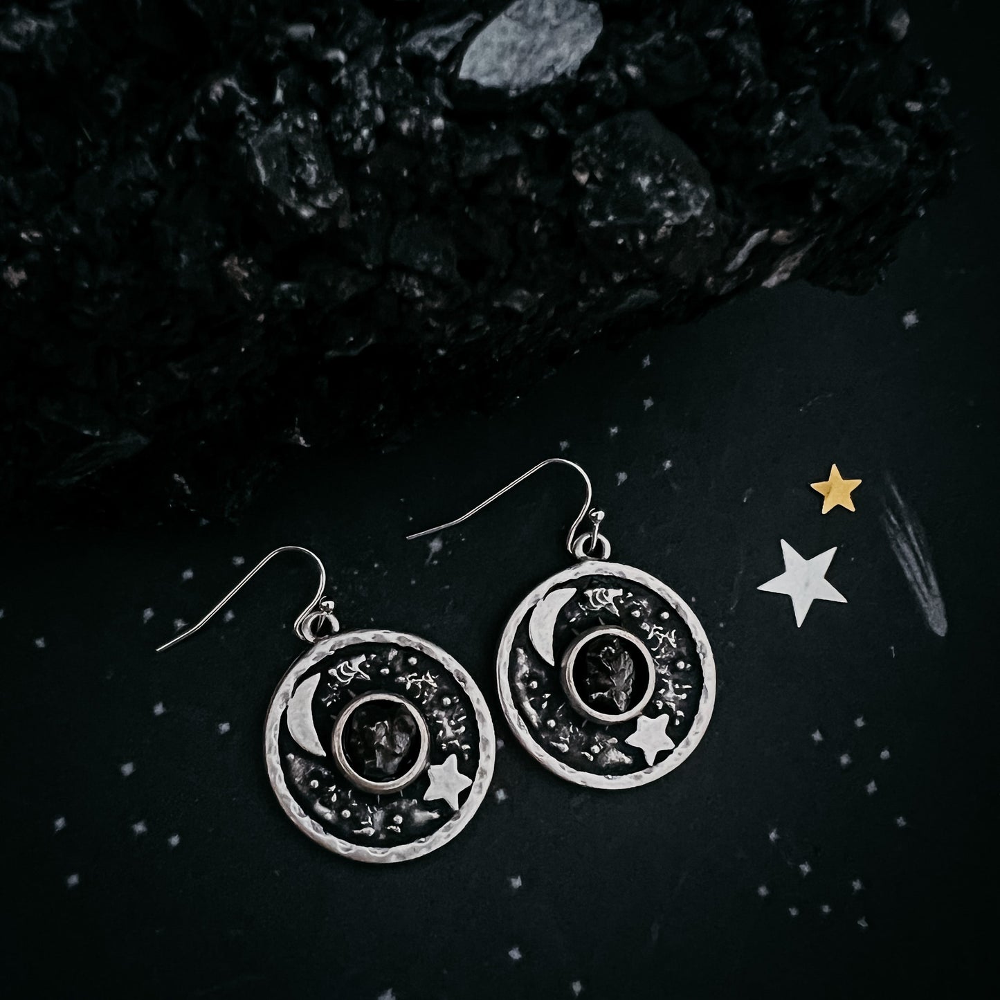 Silver earrings with celestial design on a dark background