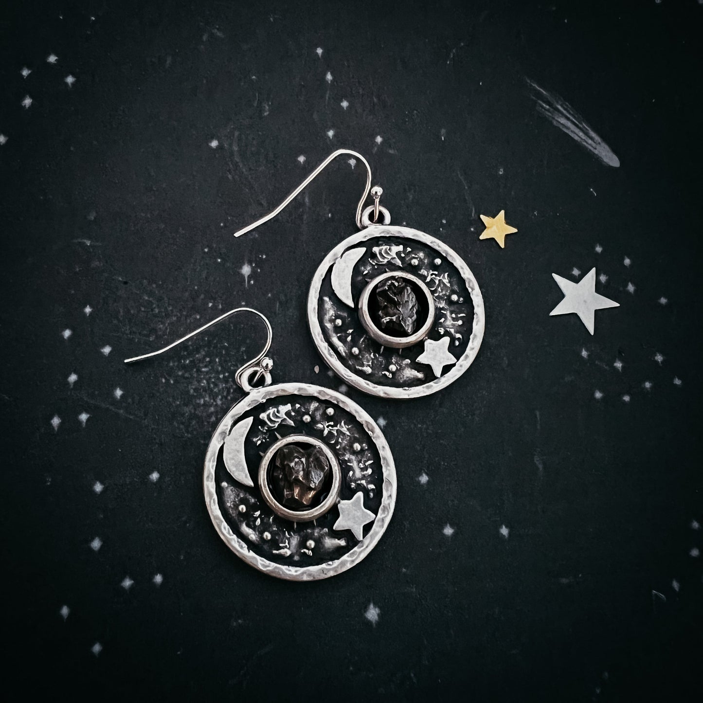 Silver earrings with celestial design on a dark background