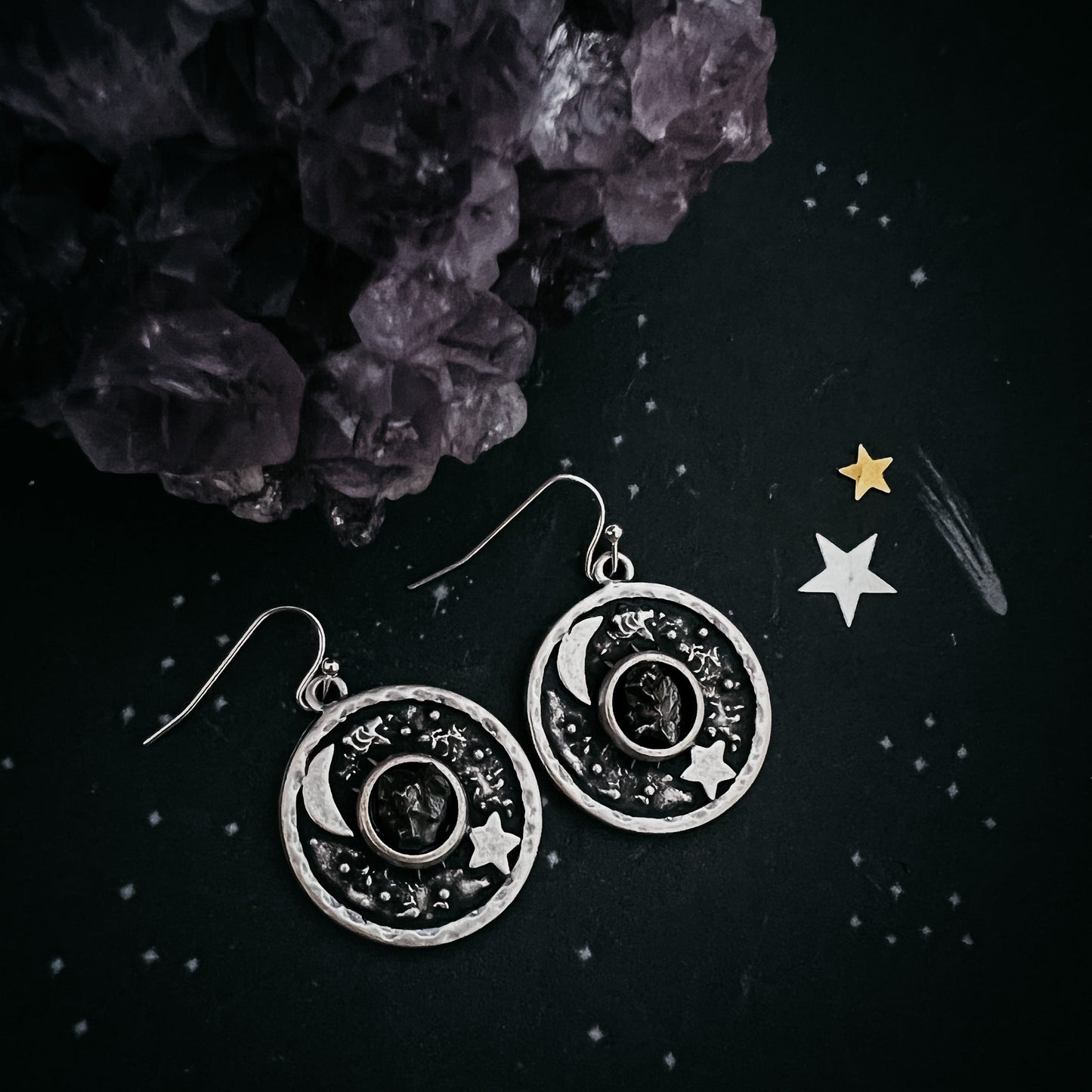 Silver celestial-themed earrings on a dark surface with decorative elements.