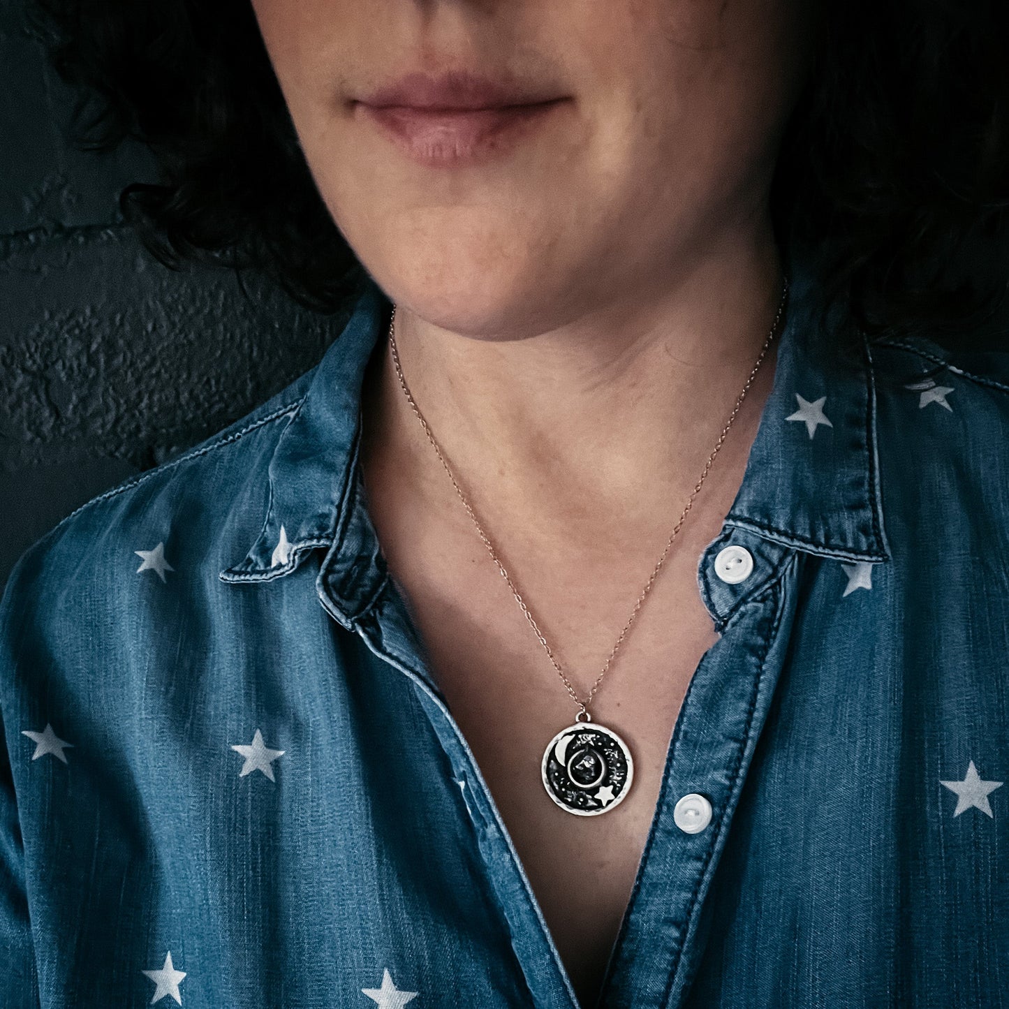 Woman wearing a blue denim shirt with star patterns and a necklace with a circular pendant.