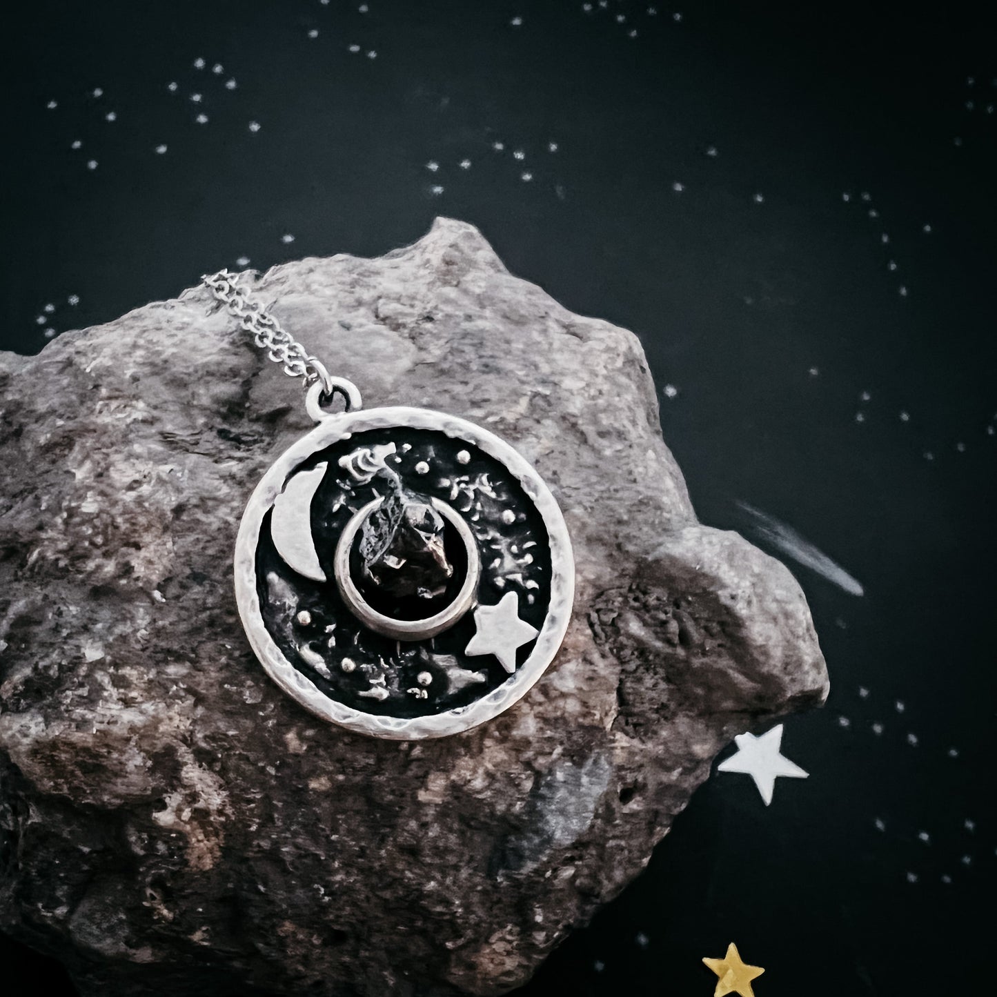 Silver necklace with a circular pendant featuring celestial designs on a rock with star decorations.