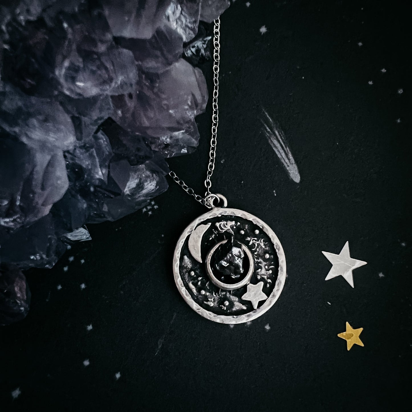Silver necklace with a circular pendant featuring celestial designs on a dark background.