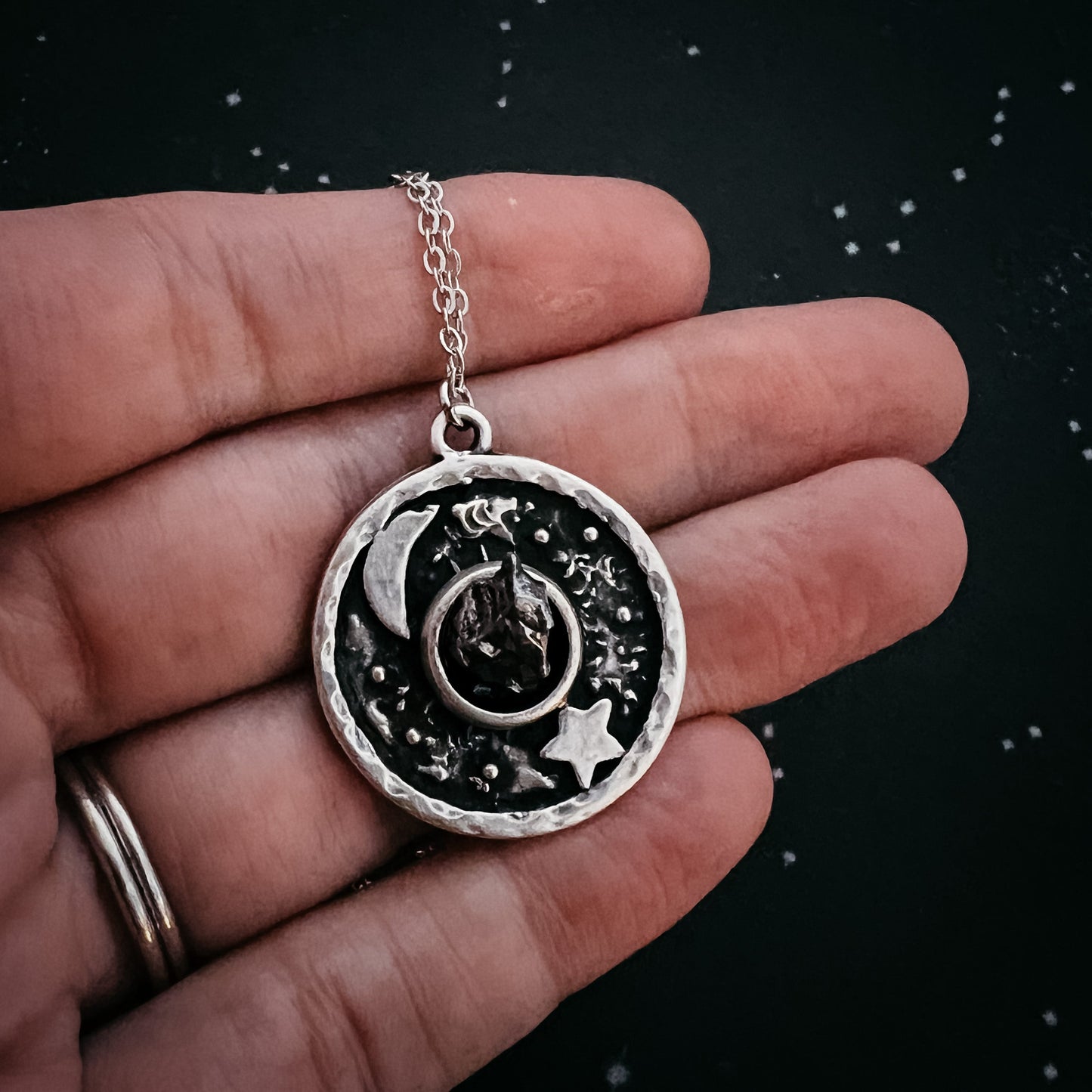 Silver necklace with a detailed pendant held in a hand against a dark background