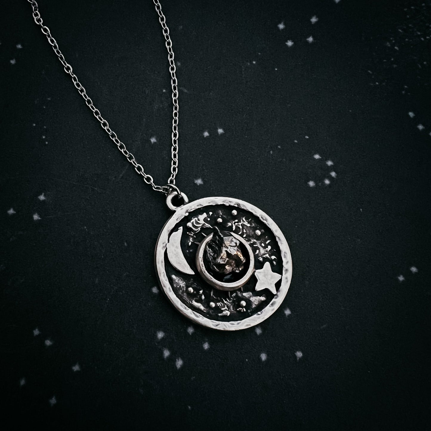 Silver necklace with a circular pendant featuring celestial designs on a black background.