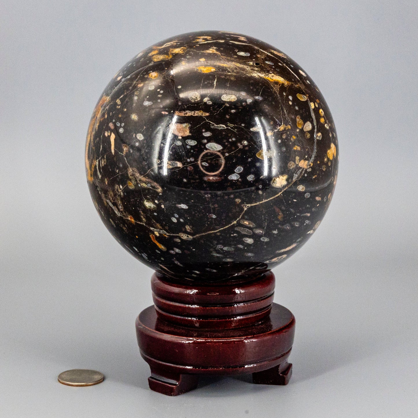 Decorative black and gold ocean jasper sphere on a wooden stand with a coin for scale.