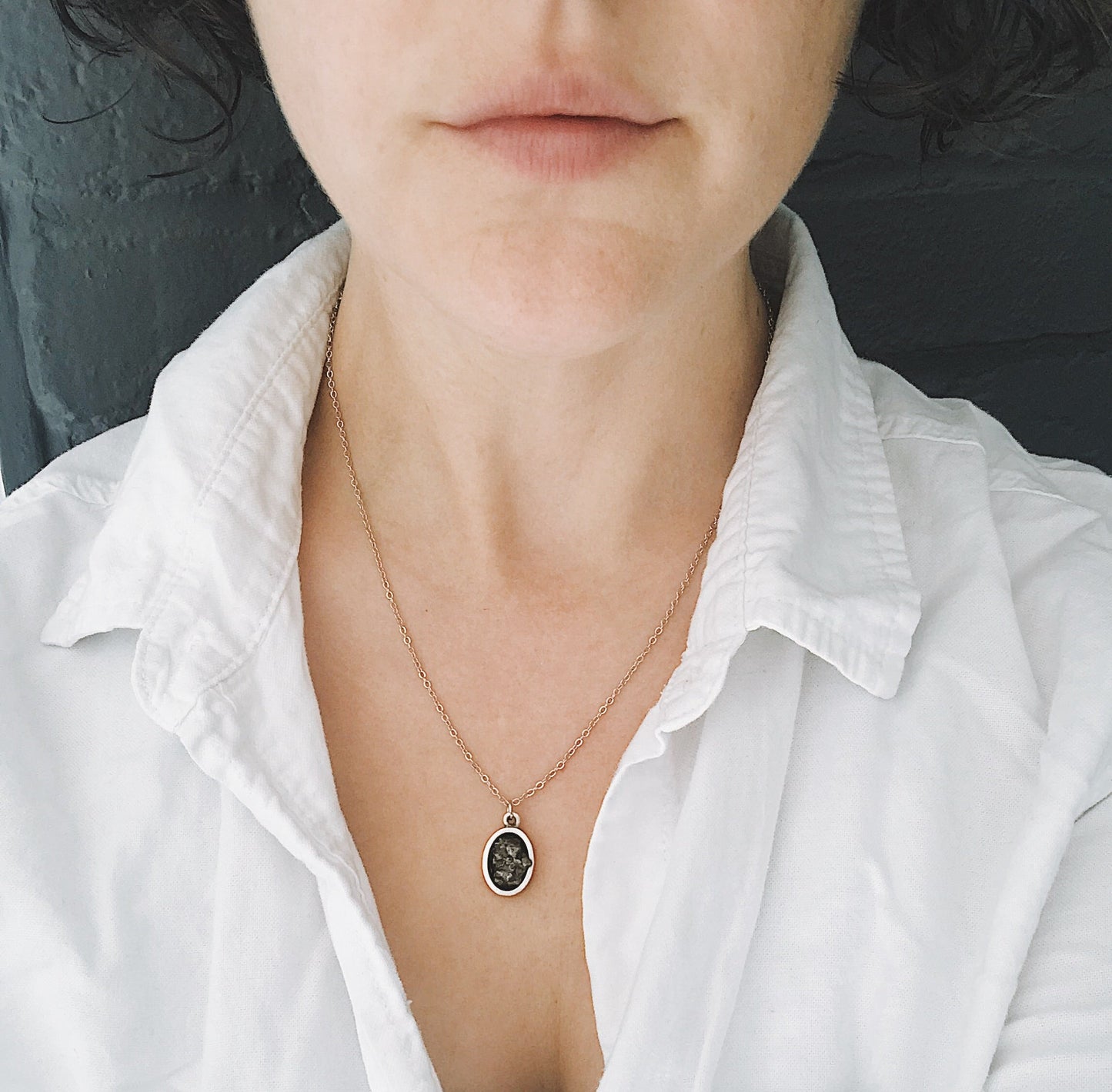 Person wearing a delicate necklace with a small pendant on a plain background