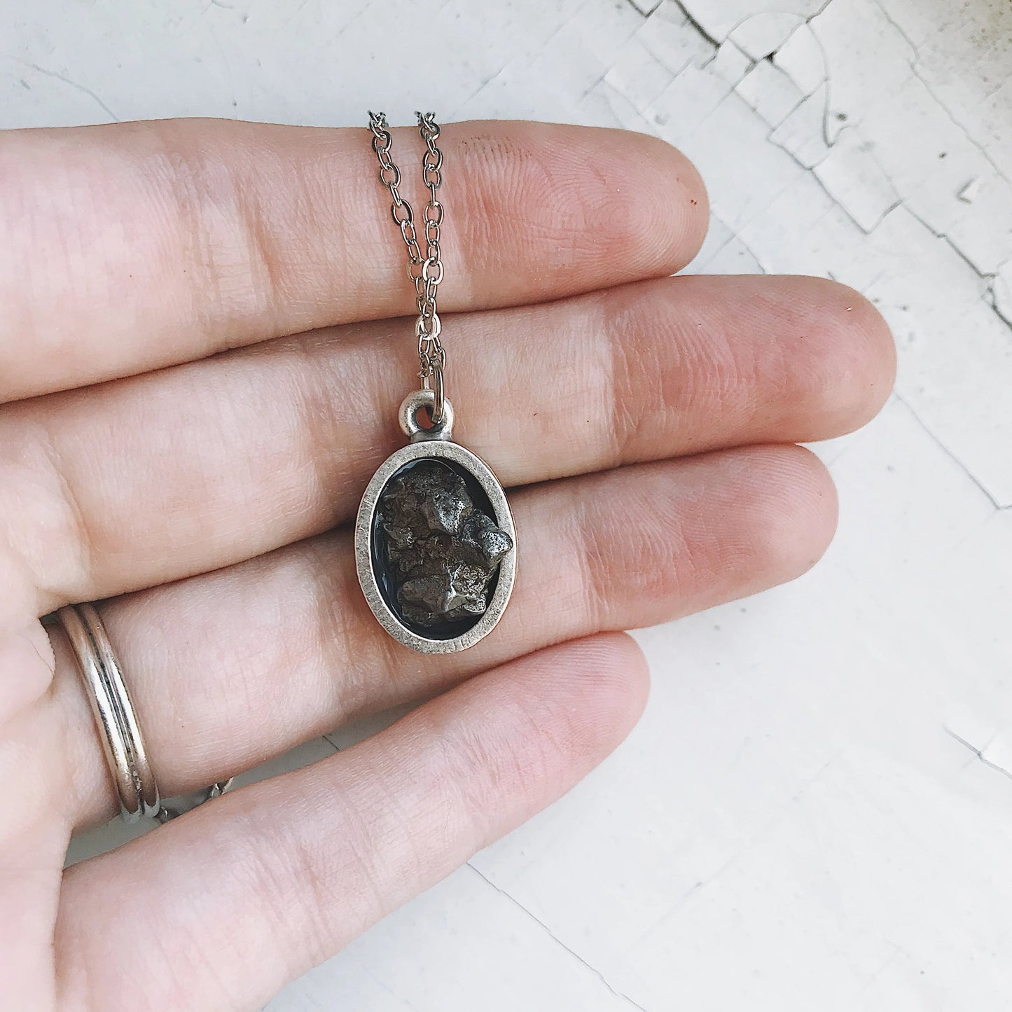 Silver pendant with meteorite held between fingers on a light background