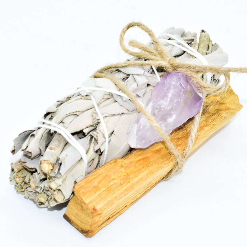 Bundled sage, palo santo, and amethyst crystal on a white background