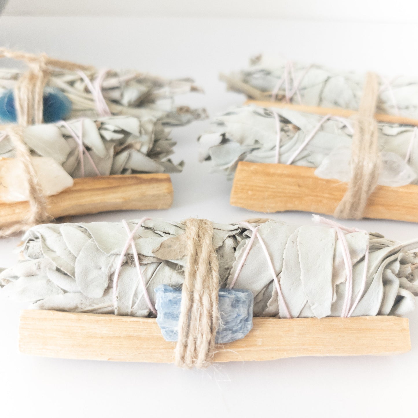 Three bundles of sage wrapped in twine with wooden handles on a white background