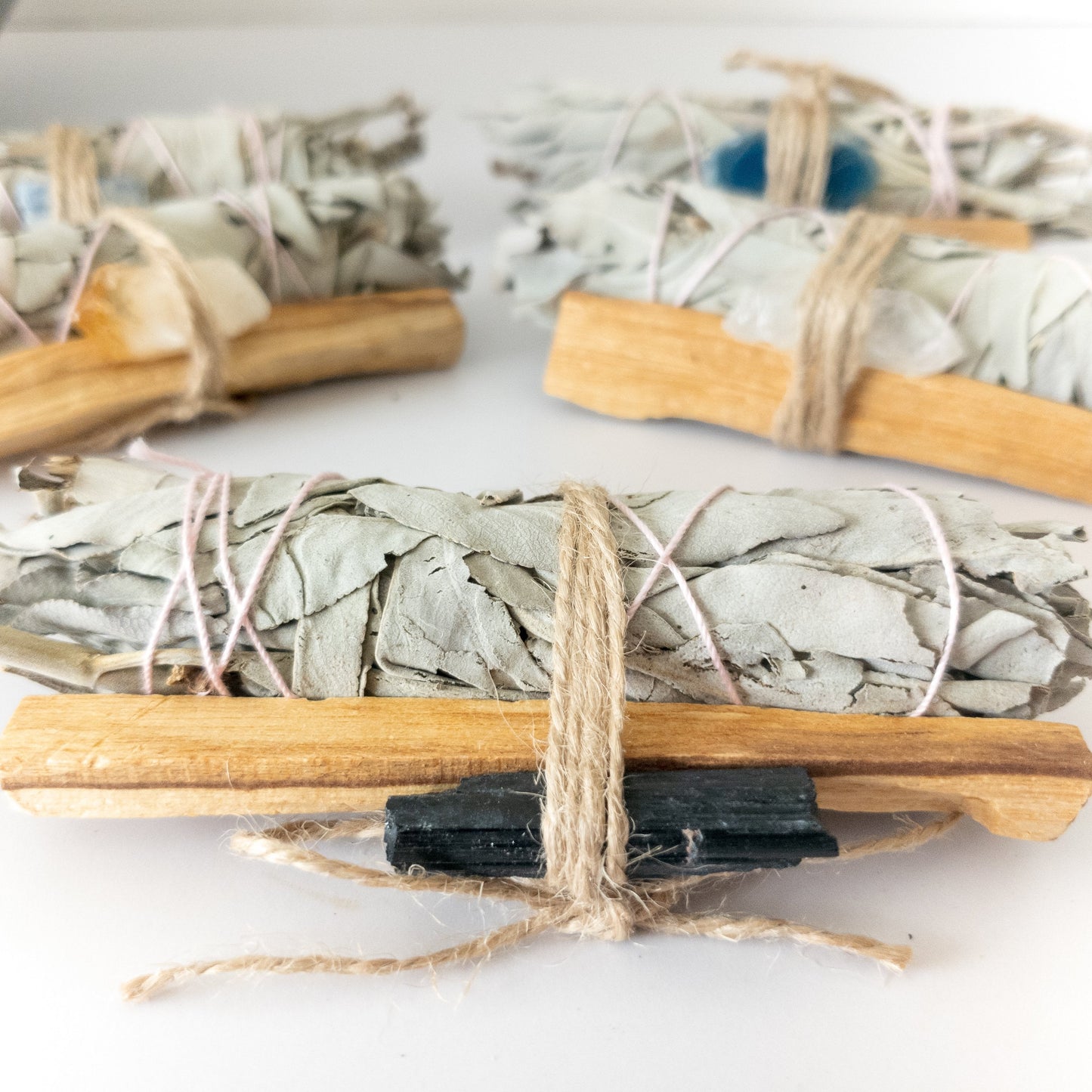 Bundles of sage, palo santo and crystals tied with twine on a white surface
