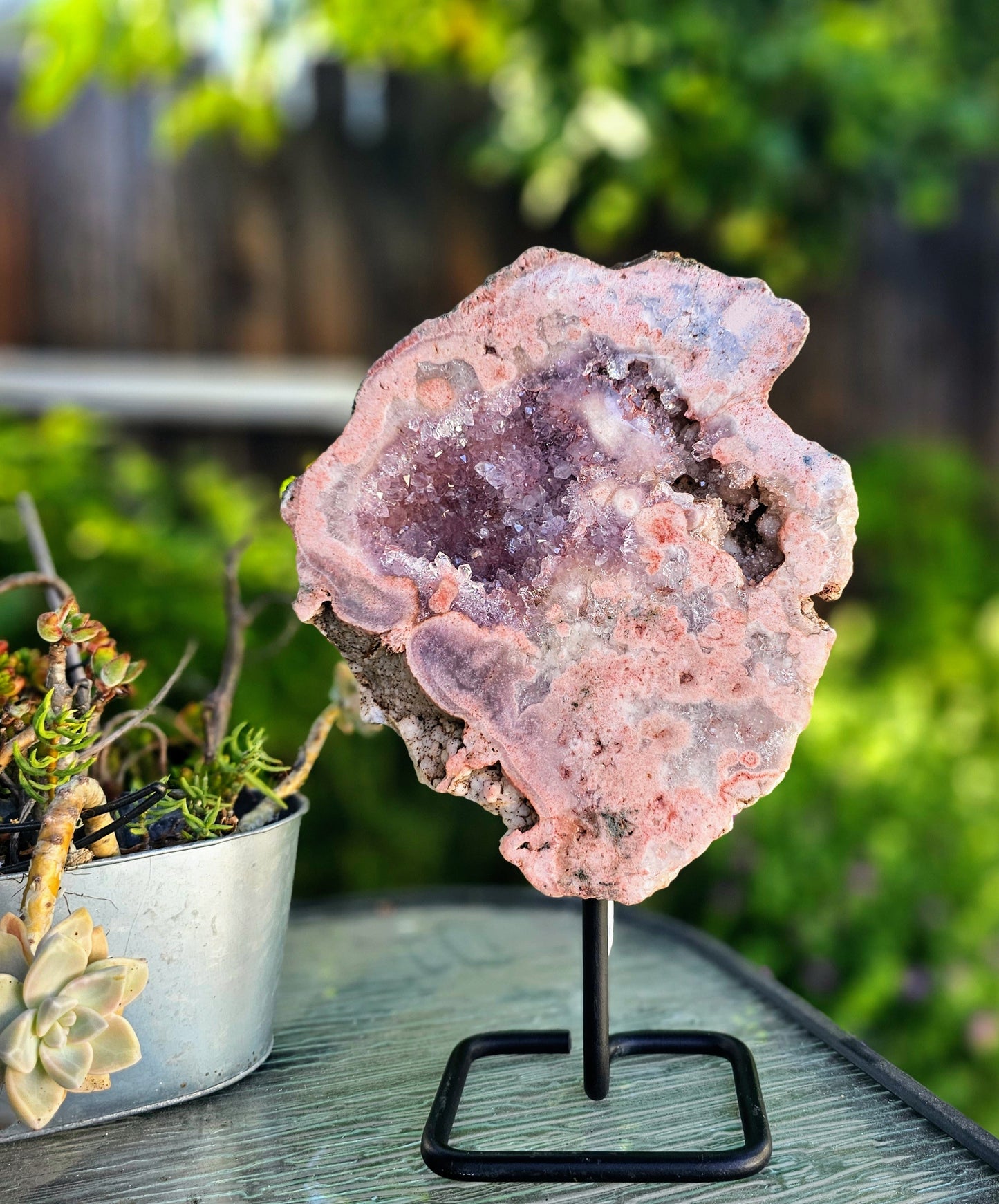 Pink crystal geode on a stand with a blurred green outdoor background