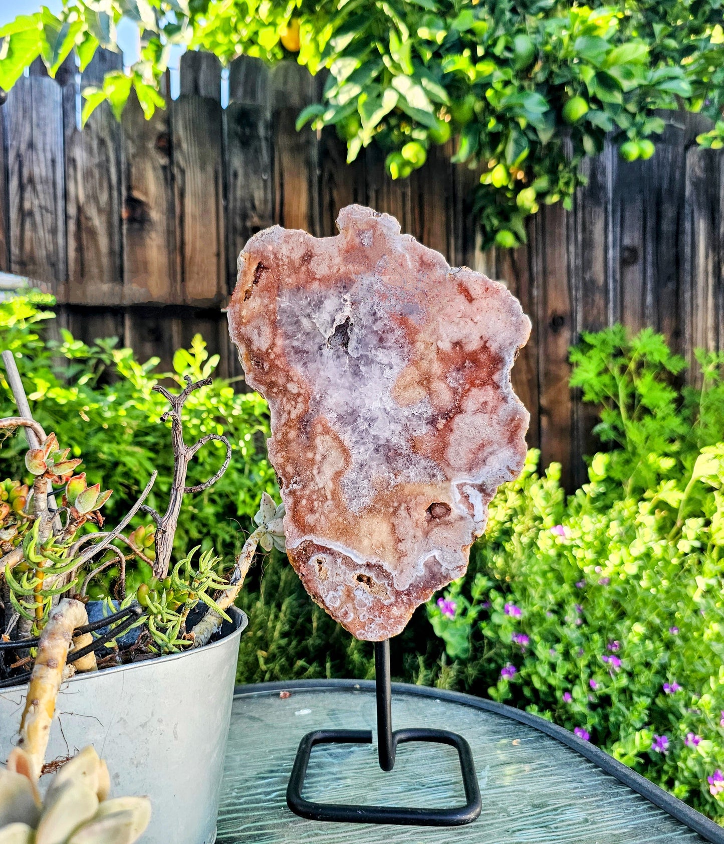 Geode crystal on a stand in a garden setting with plants and a wooden fence.