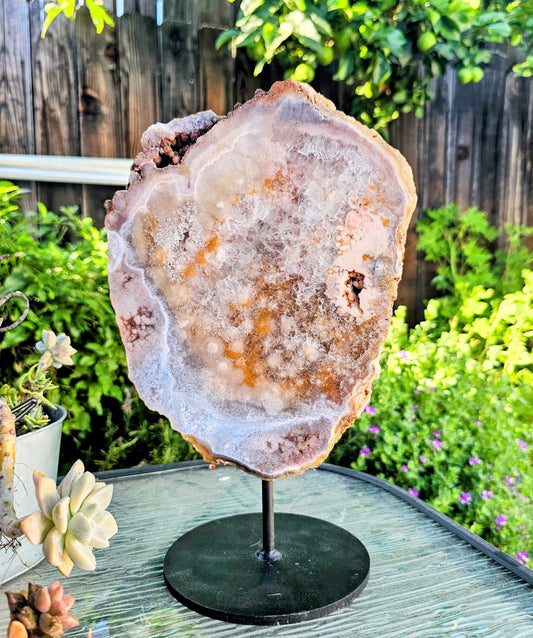 Amethyst geode on a stand outdoors with greenery in the background