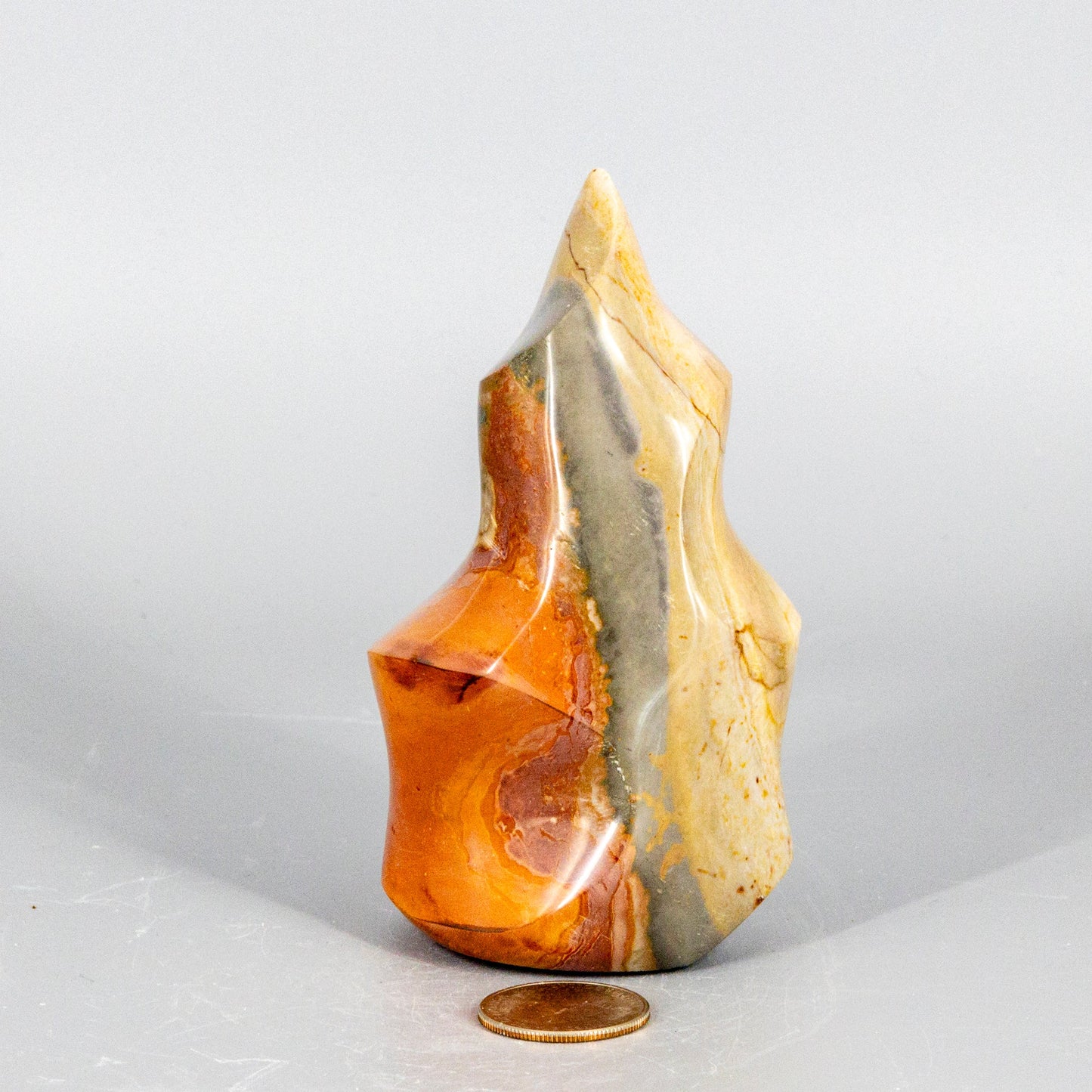 Polished polychrome jasper flame stone with a coin for scale on a light gray background