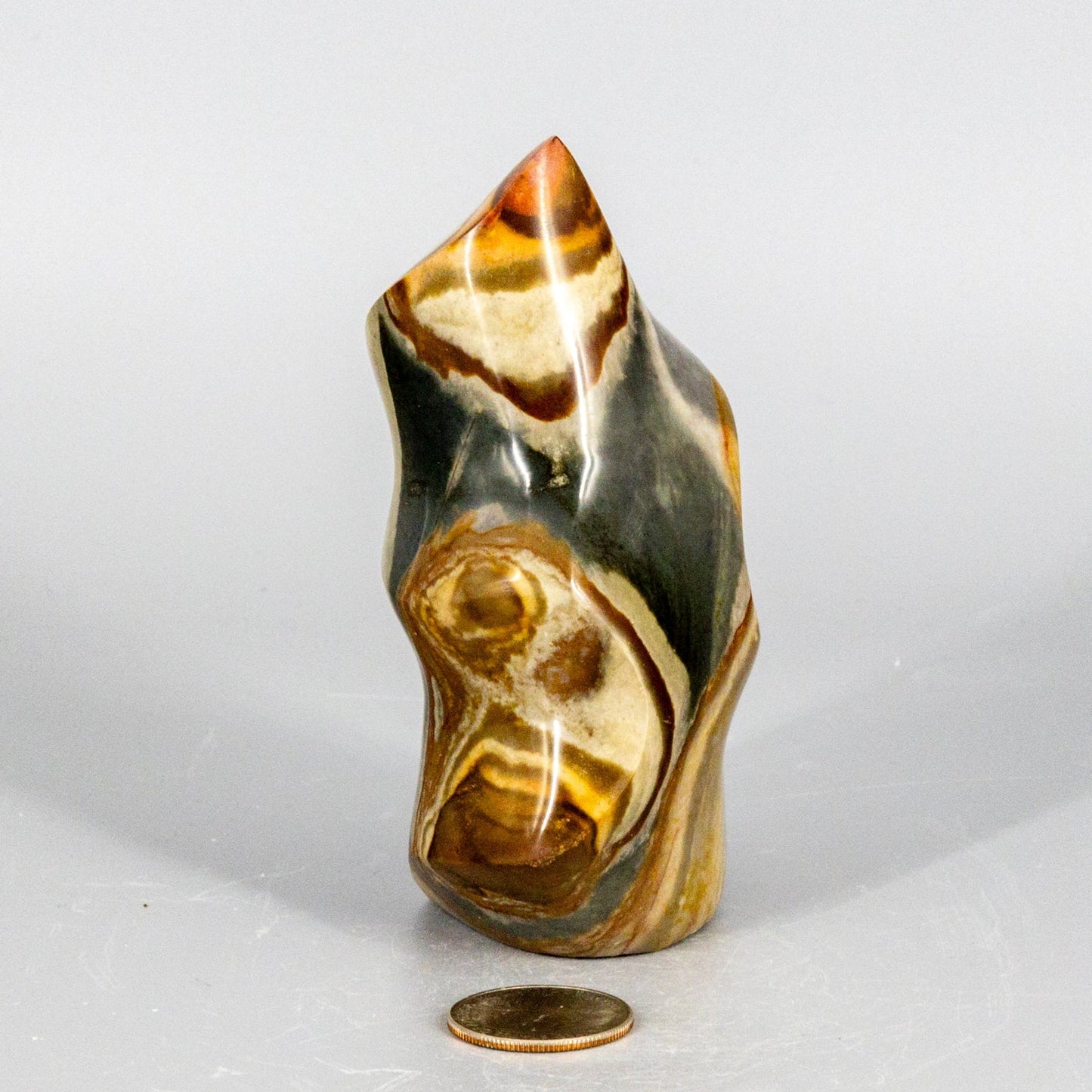 Decorative polychrome jasper flame stone with a coin for scale on a white background