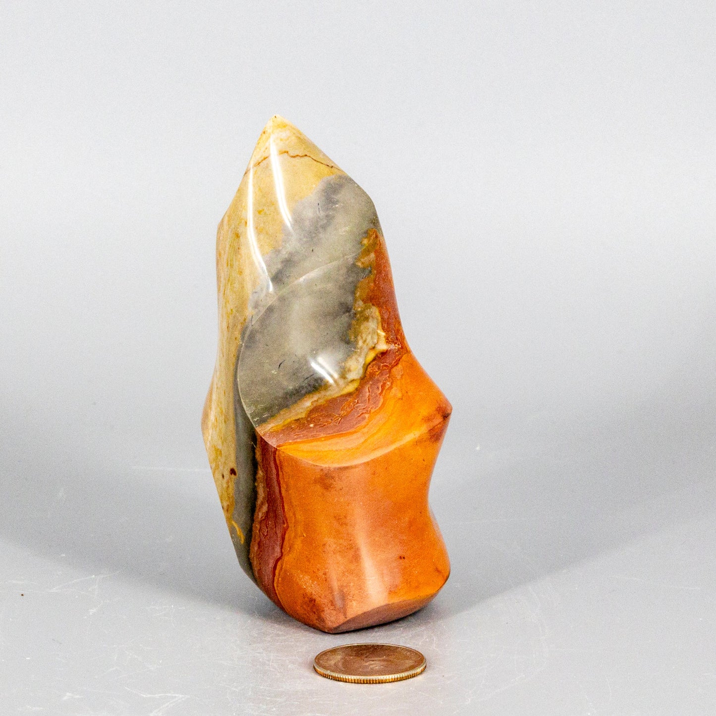 Polished orange and gray polychrome jasper flame stone with a coin for scale on a white background